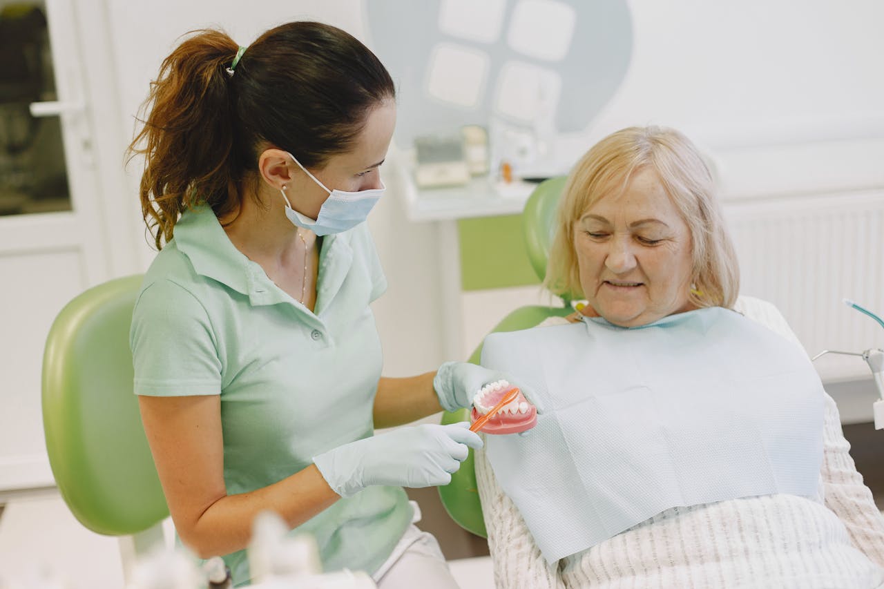 services-04 A dentist demonstrating dental health techniques to an elderly patient in a clinic.